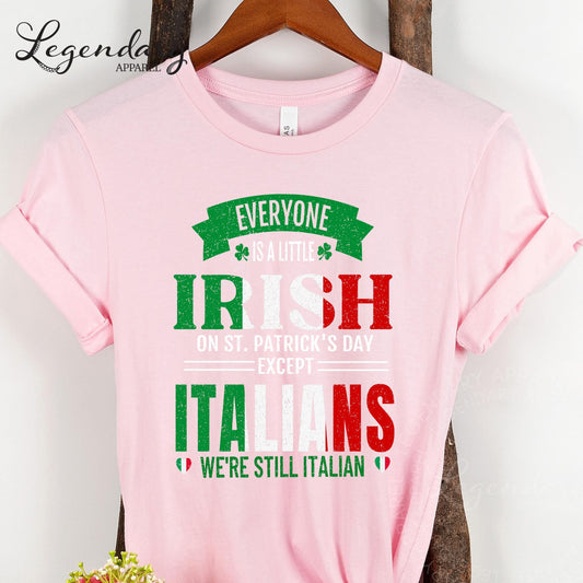 A pink t-shirt with text that reads "EVERYONE IS A LITTLE IRISH ON ST. PATRICK'S DAY EXCEPT ITALIANS WE'RE STILL ITALIAN".