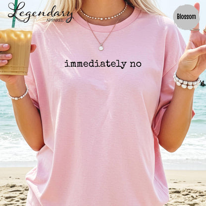 A woman wearing a pink t-shirt with the text "immediately no" printed on it, standing on a beach with her hands in her pockets.