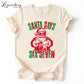 A white t-shirt with a graphic design featuring a Santa Claus figure and the text &quot;Santa says six seven&quot; in a distressed, vintage style.