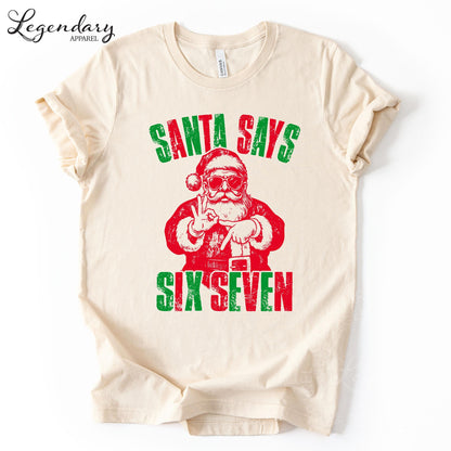 A white t-shirt with a graphic design featuring a Santa Claus figure and the text "Santa says six seven" in a distressed, vintage style.