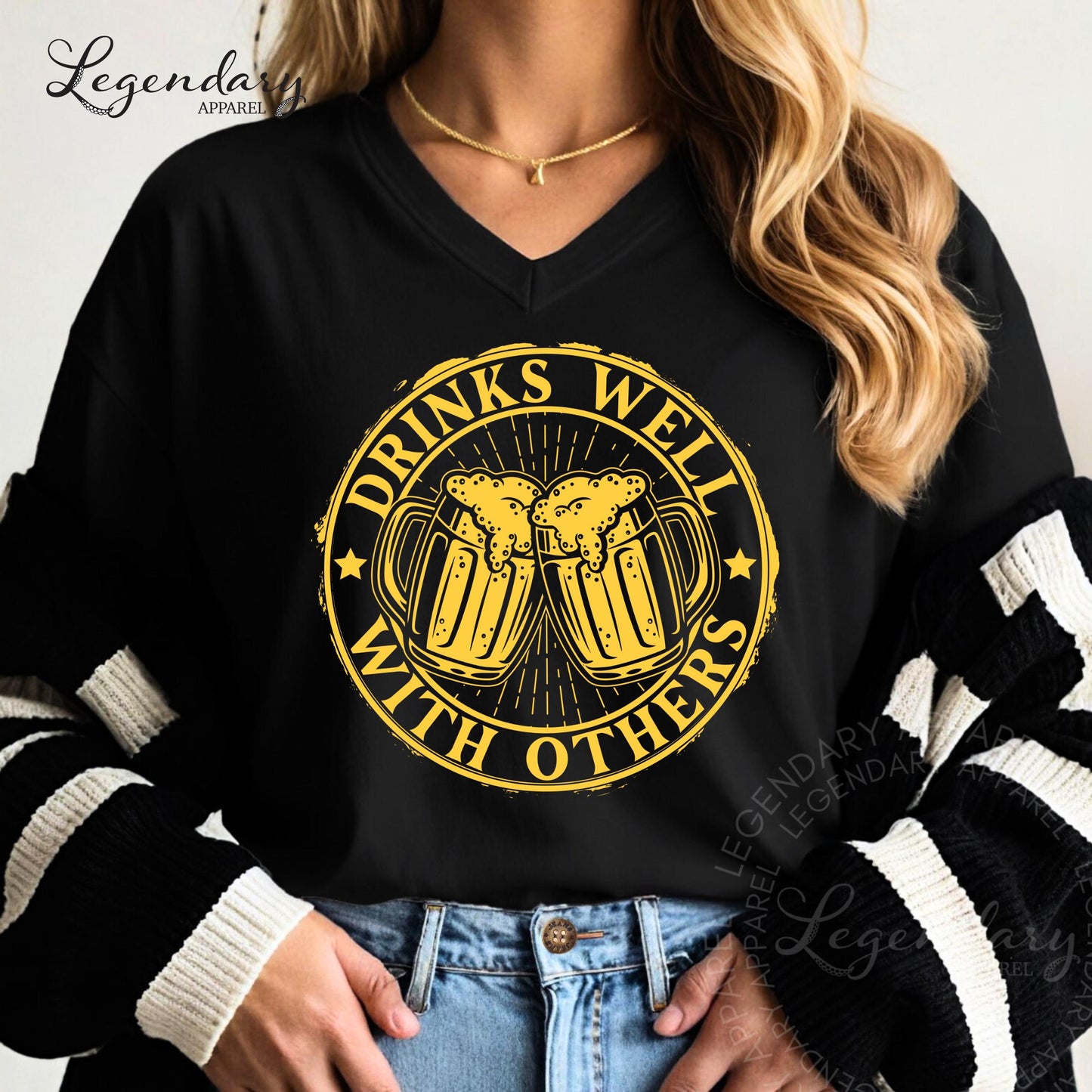 A woman wearing a black shirt with a graphic design that says "DRINKS WELL WITH OTHERS" in yellow and black.