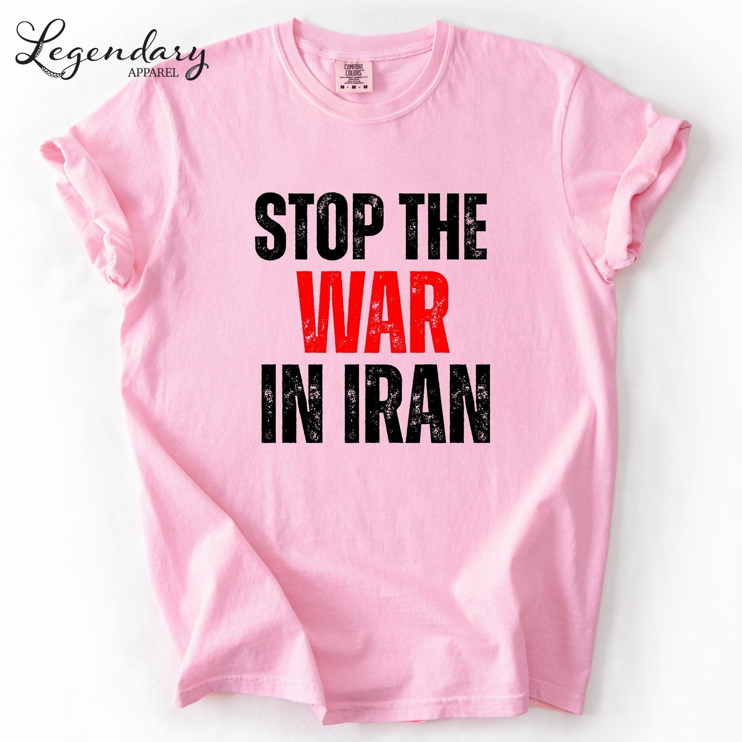 A pink t-shirt with the text "STOP THE WAR IN IRAN" printed on it in bold black letters.
