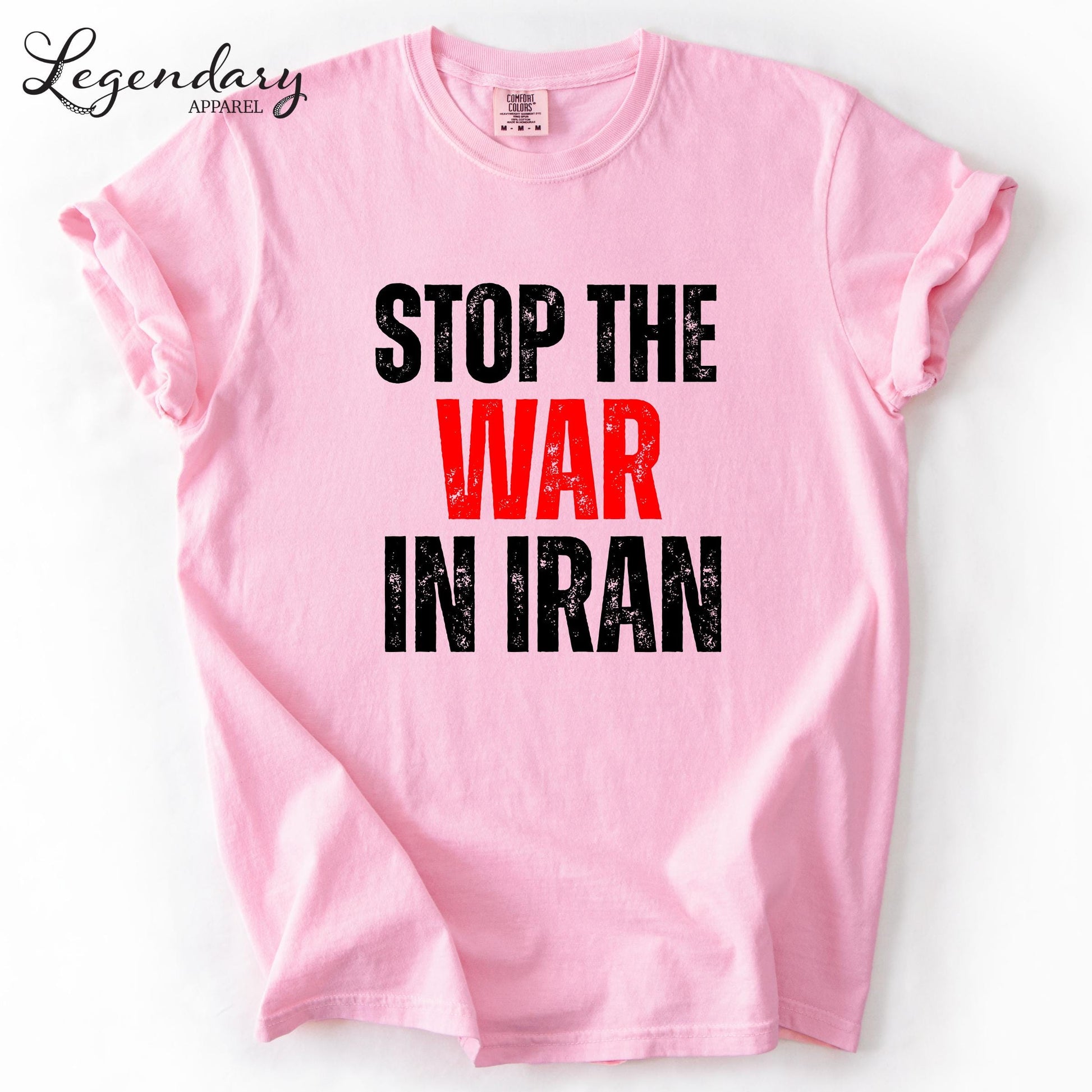 A pink t-shirt with the text "STOP THE WAR IN IRAN" printed on it in bold black letters.