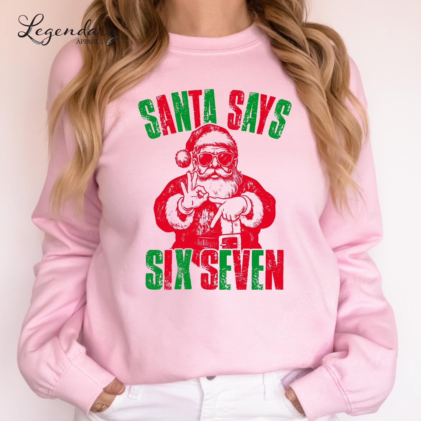 A woman wearing a pink sweatshirt with a graphic design of Santa Claus and the text &quot;Santa says six seven&quot; printed on it.