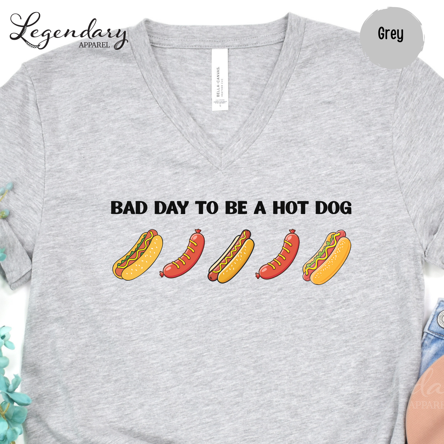A grey t-shirt with a graphic design featuring four hot dogs in different colors and styles, along with the text "Bad day to be a hot dog".