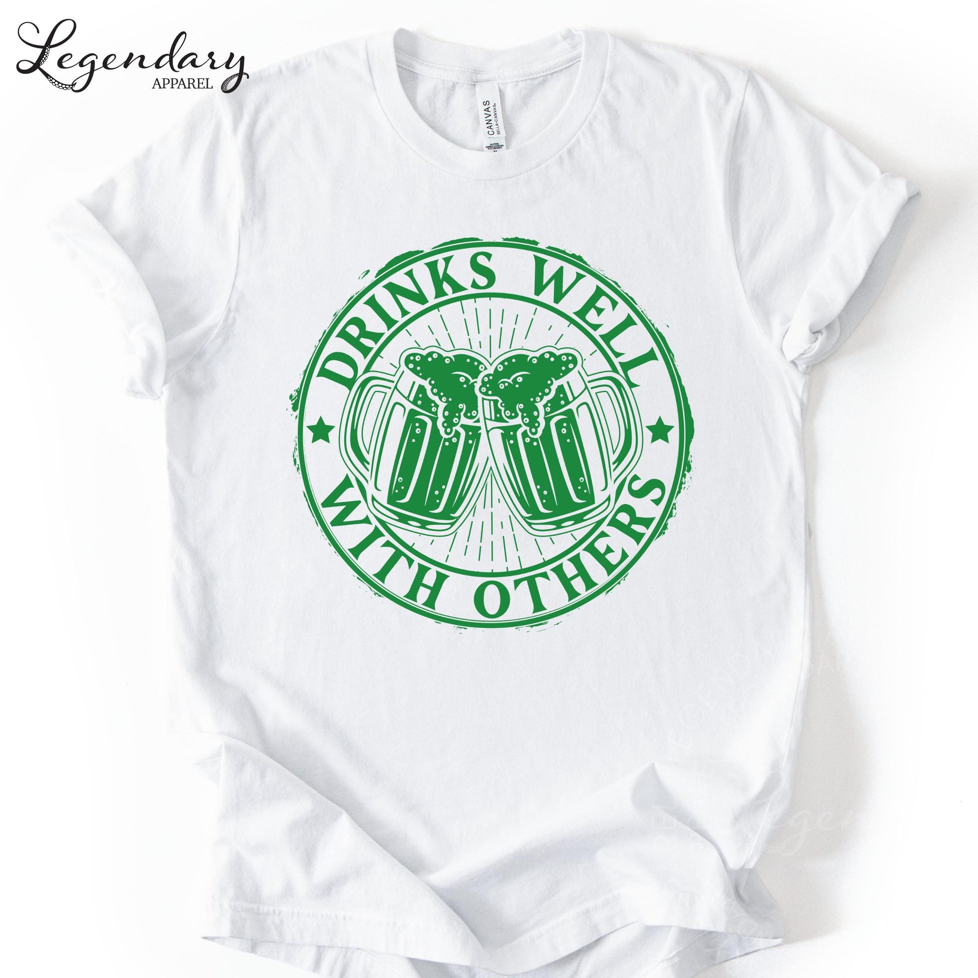 A white t-shirt with a green circular graphic design that says "DRINKS WELL WITH OTHERS" and features two beer mugs with foam on top.