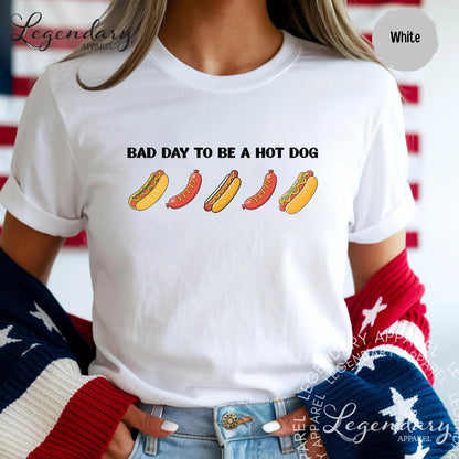 A person wearing a white t-shirt with the text "Bad day to be a hot dog" printed on it, along with four hot dogs in different colors.