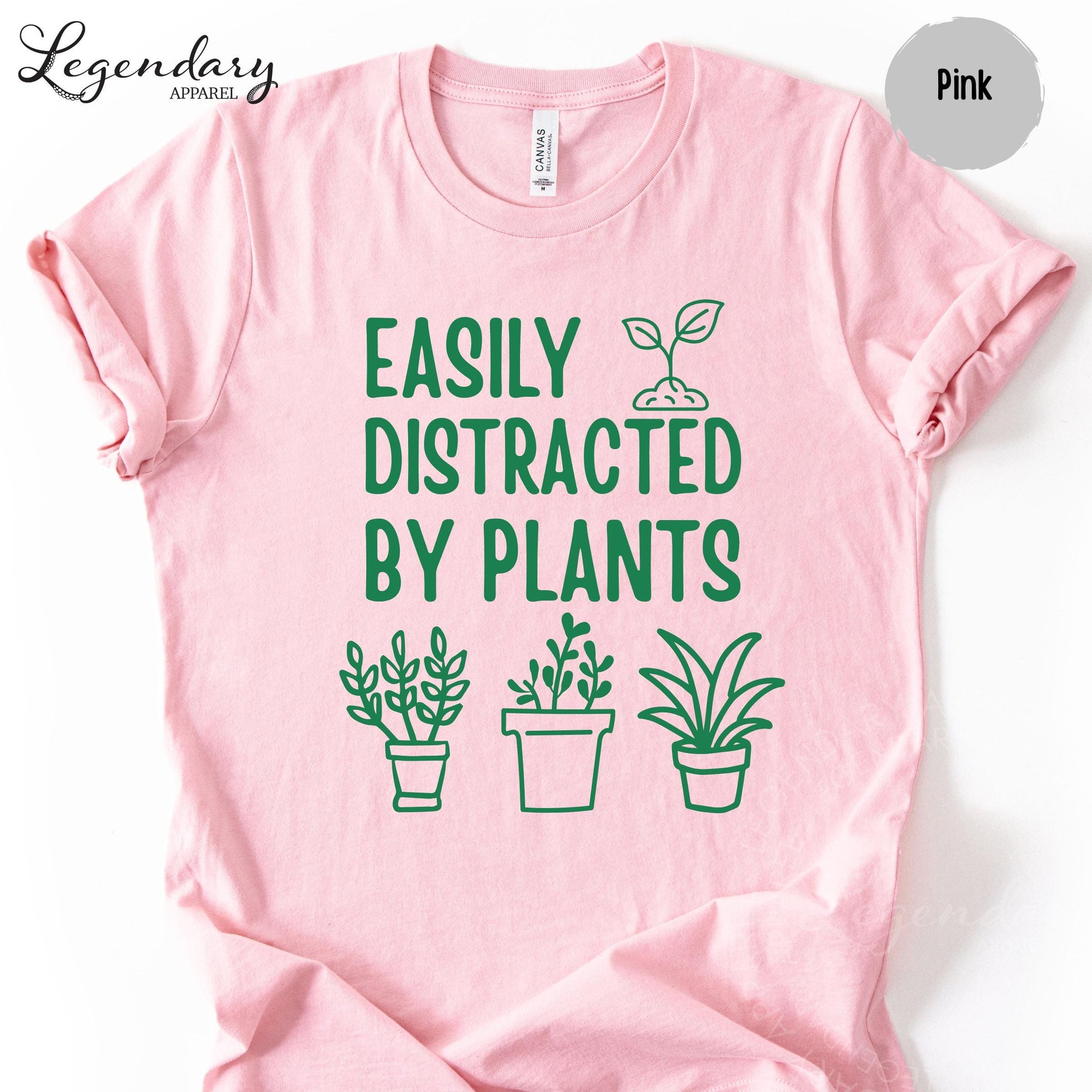 A pink t-shirt with a graphic design featuring a plant and the text "EASILY DISTRACTED BY PLANTS" printed on it.
