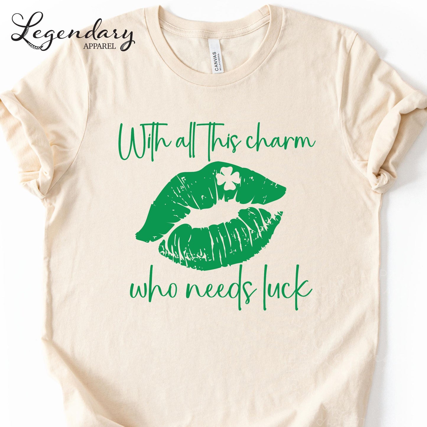 A beige t-shirt with a graphic design featuring green lips and a clover leaf, along with the text "With all this charm who needs luck".