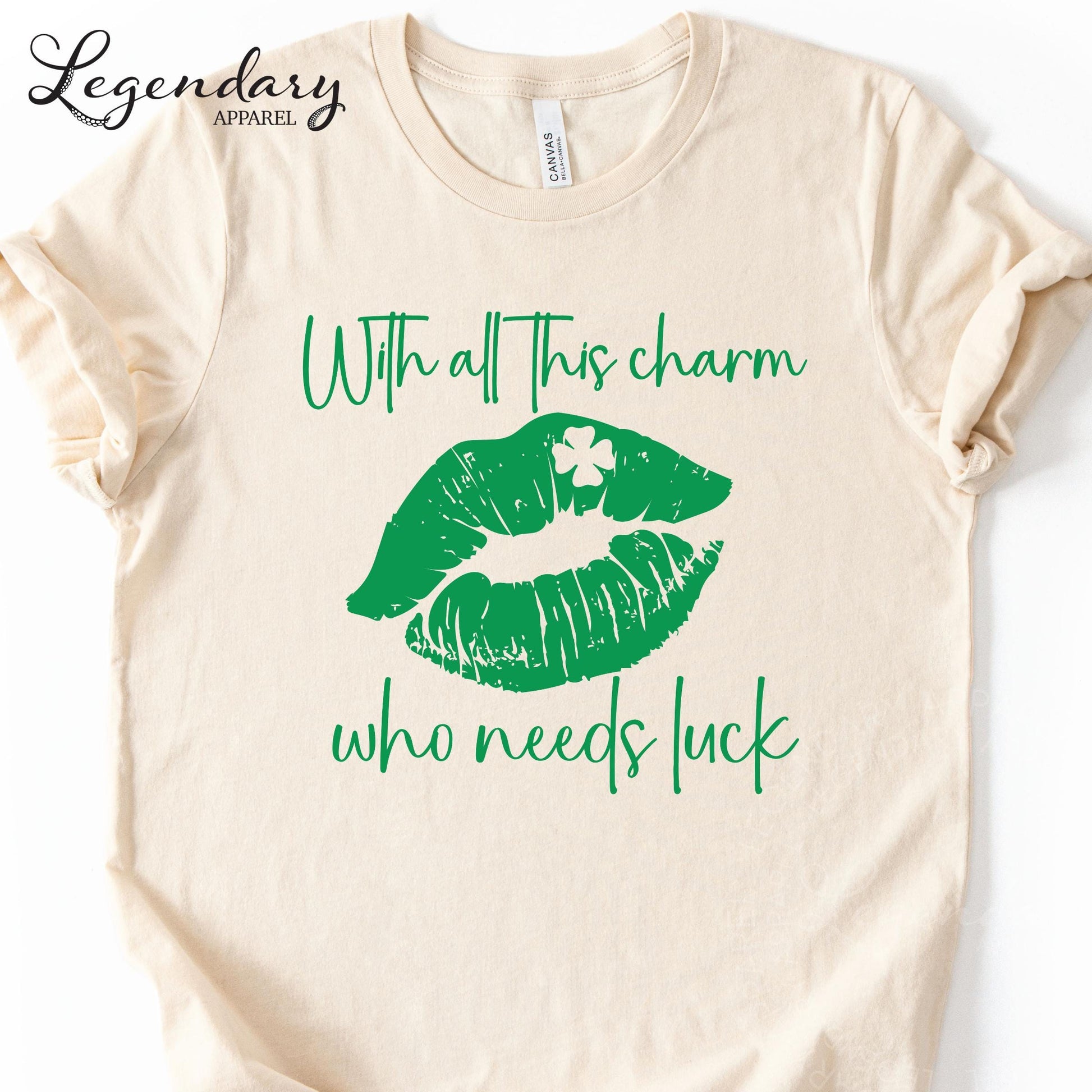 A beige t-shirt with a graphic design featuring green lips and a clover leaf, along with the text "With all this charm who needs luck".