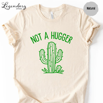 A beige t-shirt with a green graphic design depicting a cactus and the text "NOT A HUGGER" printed on it.