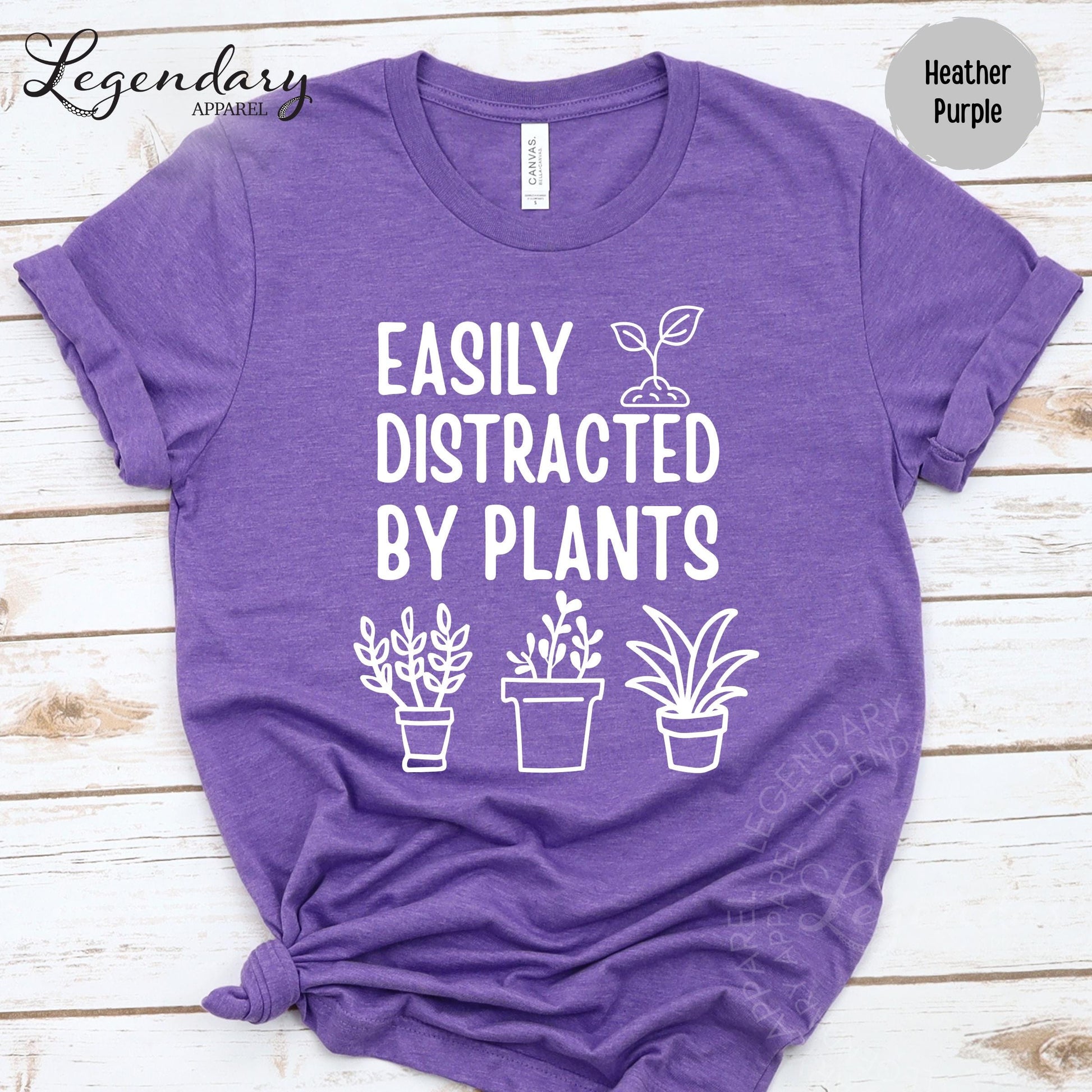 A purple t-shirt with the text "EASILY DISTRACTED BY PLANT" printed on it, along with three simple illustrations of potted plants.