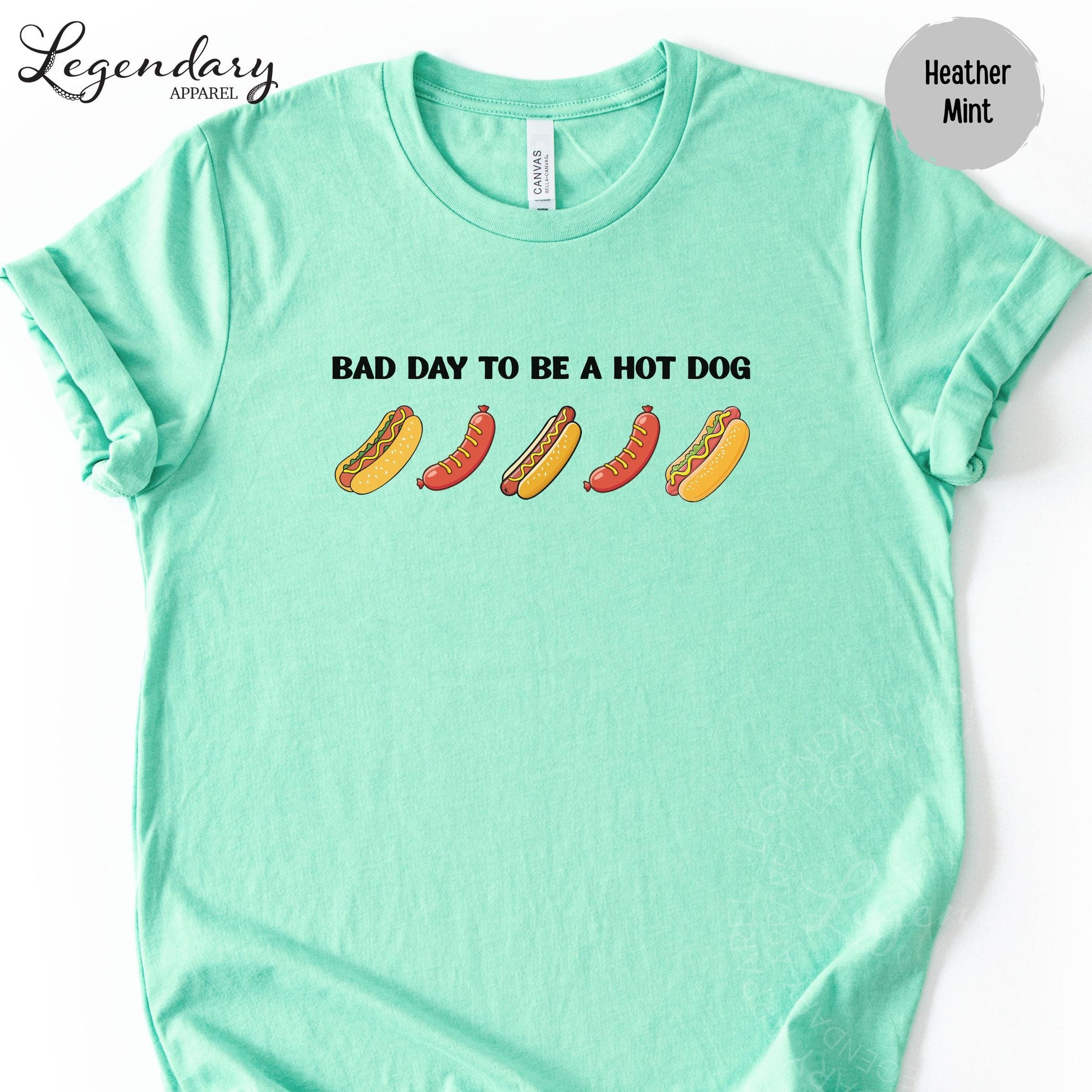 A mint green t-shirt with the text "Bad day to be a hot dog" printed on it, along with illustrations of hot dogs.