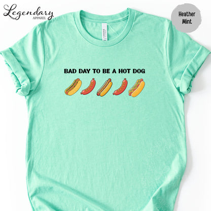 A mint green t-shirt with the text "Bad day to be a hot dog" printed on it, along with illustrations of hot dogs.