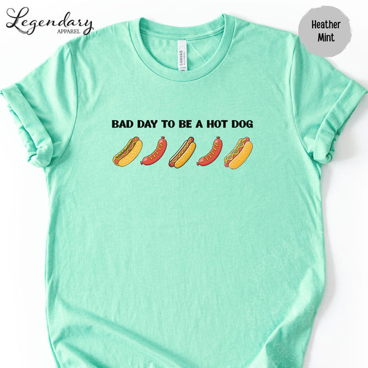 A mint green t-shirt with the text "Bad day to be a hot dog" printed on it, along with illustrations of hot dogs.