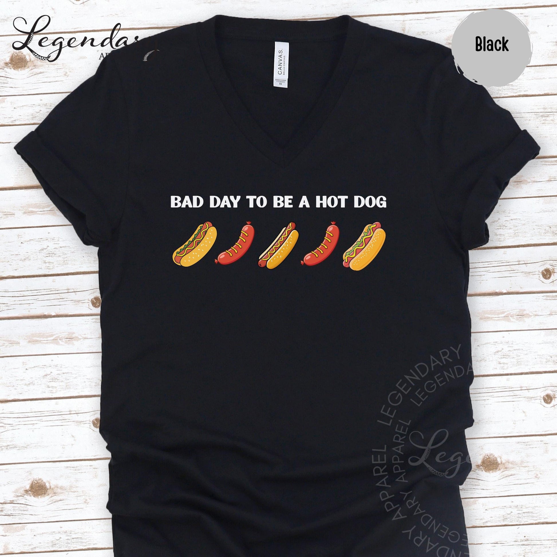 A black t-shirt with a graphic design featuring a line of hot dogs in various colors, accompanied by the text "Bad day to be a hot dog".