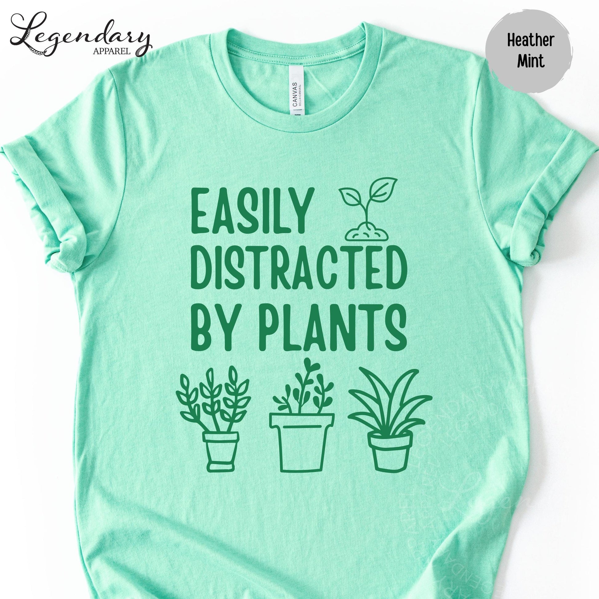 A mint green t-shirt with the text "EASILY DISTRACTED BY PLANTS" printed on it, along with three simple plant illustrations.