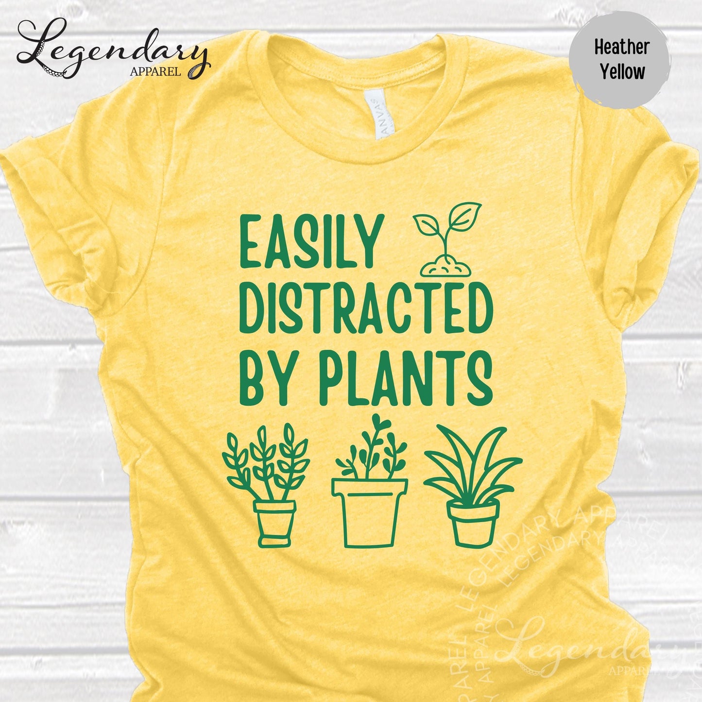 The image is a yellow t-shirt with a graphic design featuring a plant and the text "EASILY DISTRACTED BY PLANTS" printed on it.