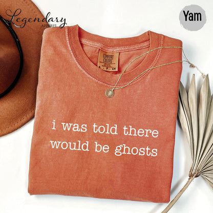 a red t-shirt with the text "I was told there would be ghosts" printed on it, along with a necklace and a hat.