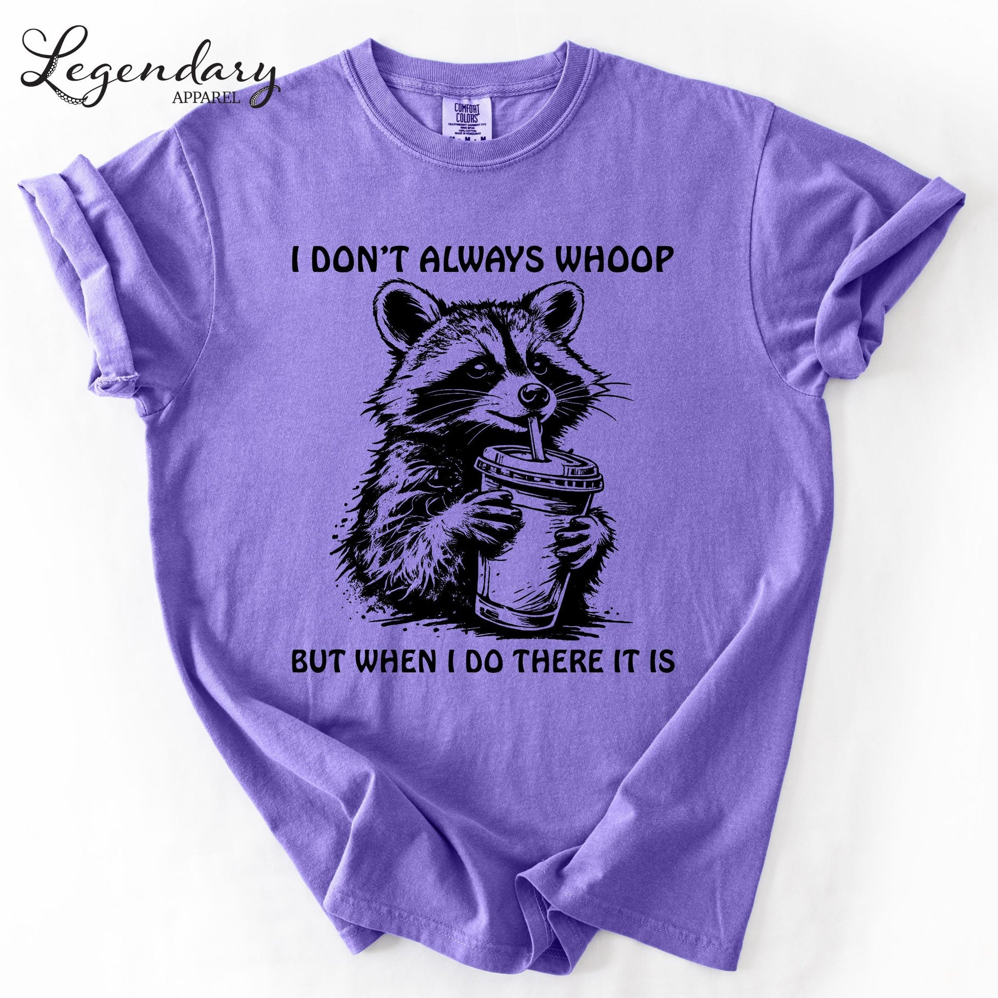 A purple t-shirt with a graphic design depicting a raccoon holding a cup, accompanied by the text "I DON'T ALWAYS WHOOP BUT WHEN I DO THERE IT IS".
