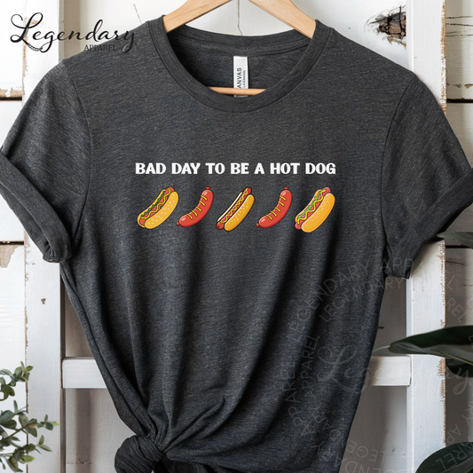 A gray t-shirt with a graphic design featuring four hot dogs in different colors and styles, along with the text "Bad day to be a hot dog".
