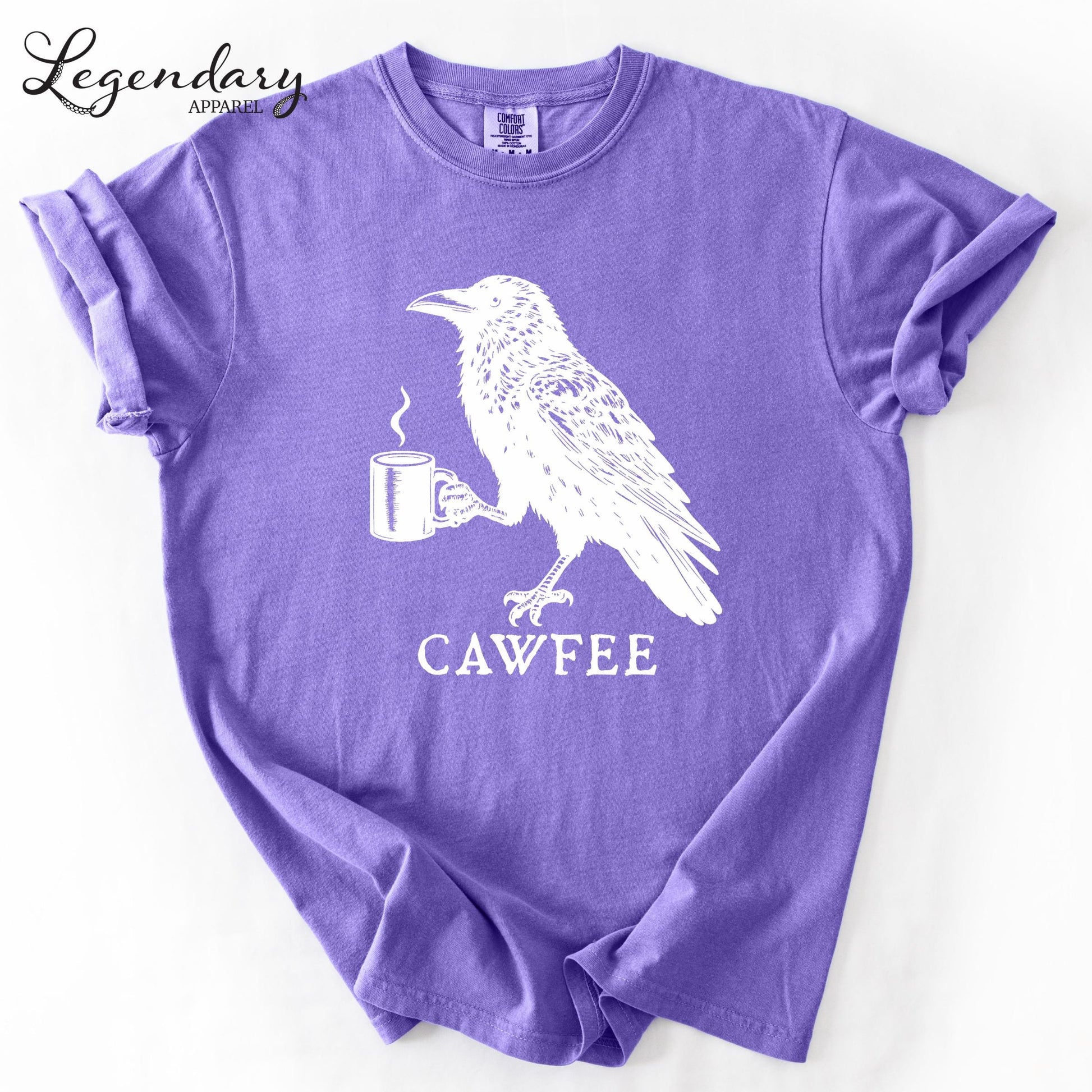 A purple t-shirt with a white illustration of a bird holding a cup of coffee, accompanied by the text "CAWFREE".