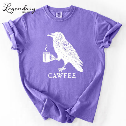 A purple t-shirt with a white illustration of a bird holding a cup of coffee, accompanied by the text "CAWFREE".