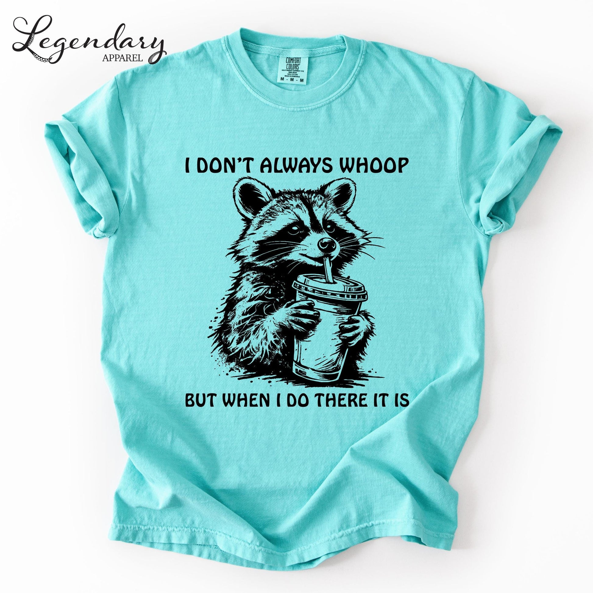 A turquoise t-shirt with a graphic of a raccoon holding a drink and the text "I DON'T ALWAYS WHOOP BUT WHEN I DO THERE IT IS" printed on it.