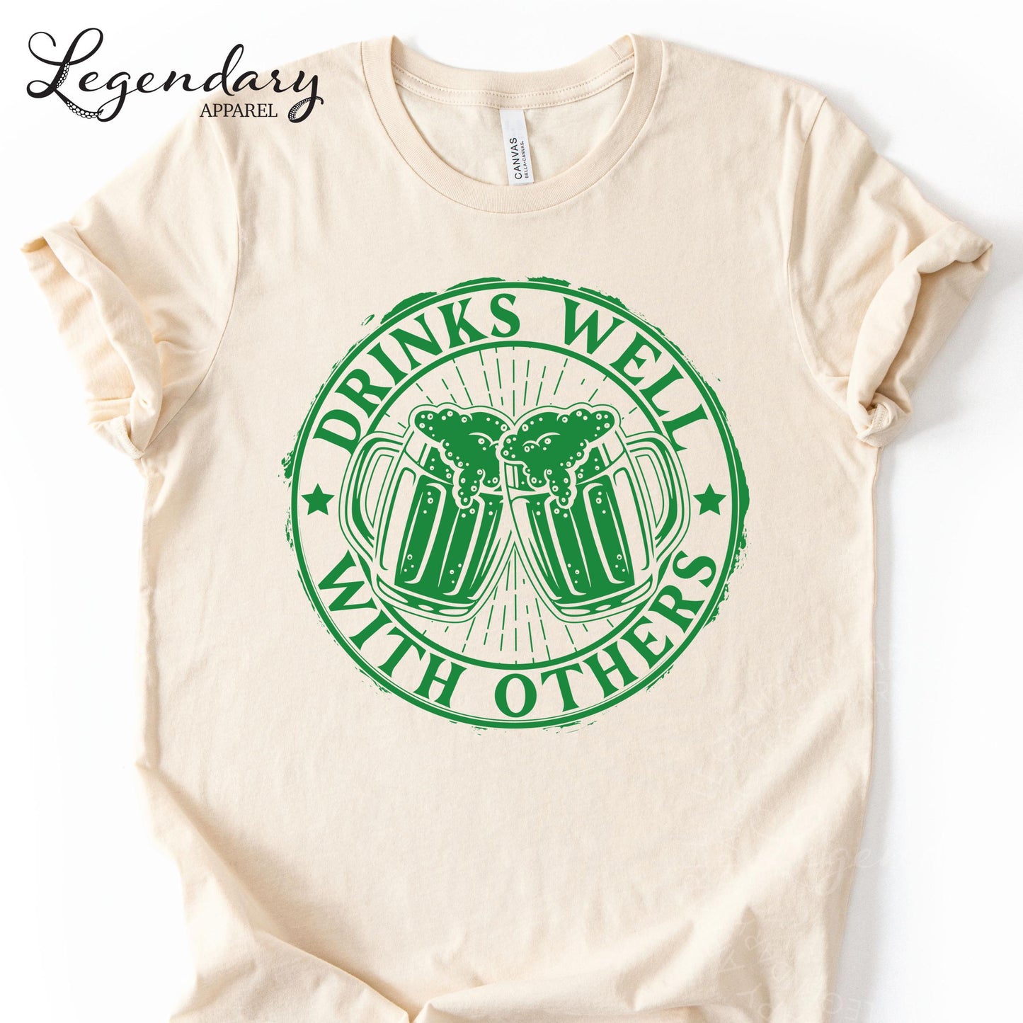 a white t-shirt with a green graphic design on it. The design consists of two beer mugs with a text that reads "DRINKS WELL WITH OTHERS".