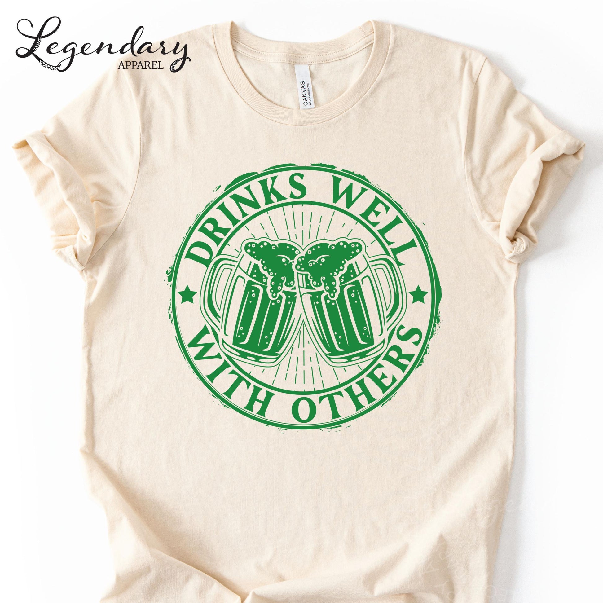 a white t-shirt with a green graphic design on it. The design consists of two beer mugs with a text that reads "DRINKS WELL WITH OTHERS".