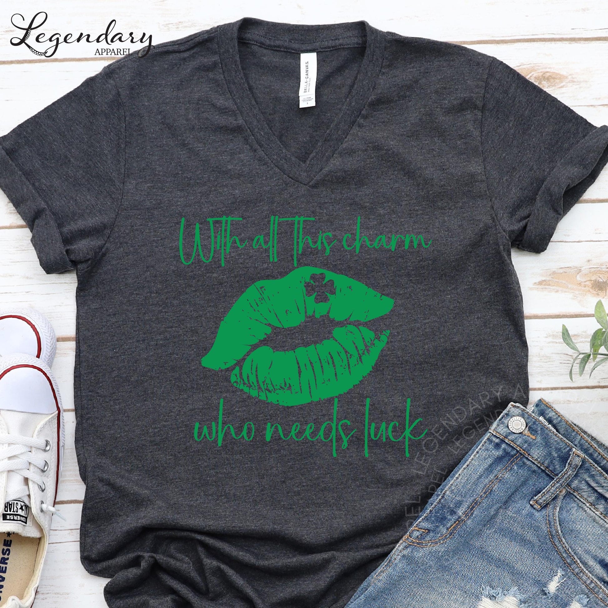 A gray t-shirt with a green graphic design and text printed on it, along with a pair of jeans and a pair of sneakers.