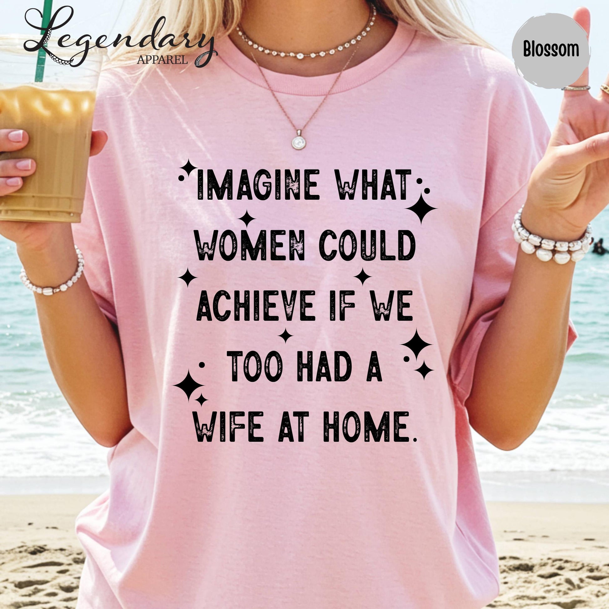 A woman wearing a pink t-shirt with a humorous text printed on it, standing on a beach with the ocean in the background.