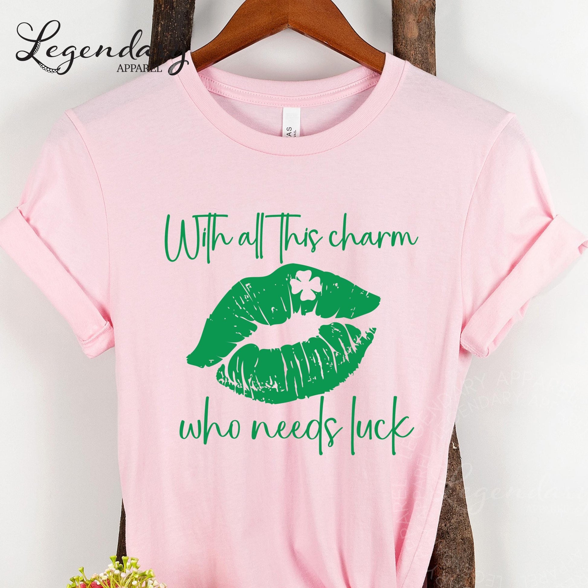 A pink t-shirt with a graphic design of green lips and a white clover, along with the text "With all this charm who needs luck" printed on it.