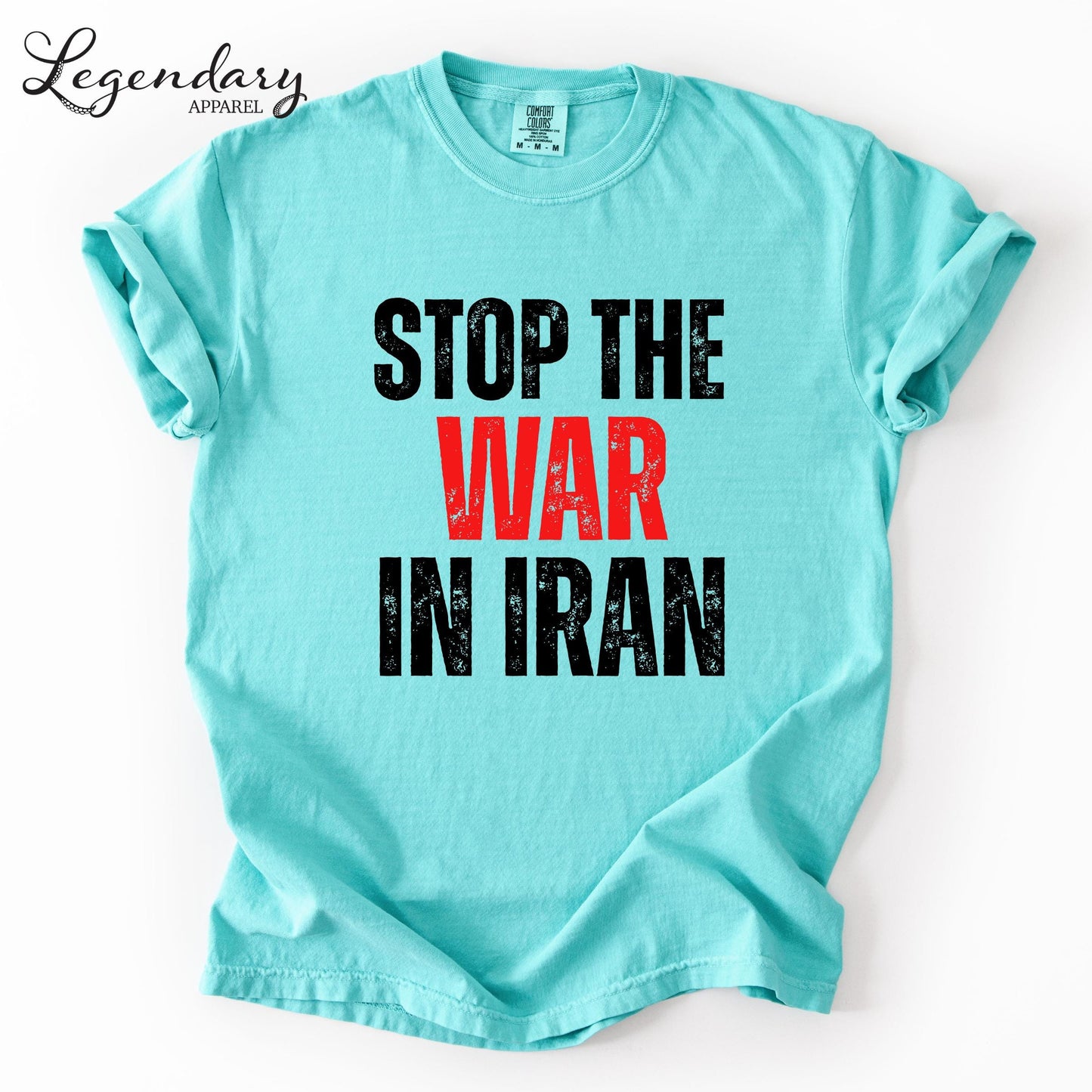 A turquoise t-shirt with the text "STOP THE WAR IN IRAN" printed on it in bold, black and red letters.