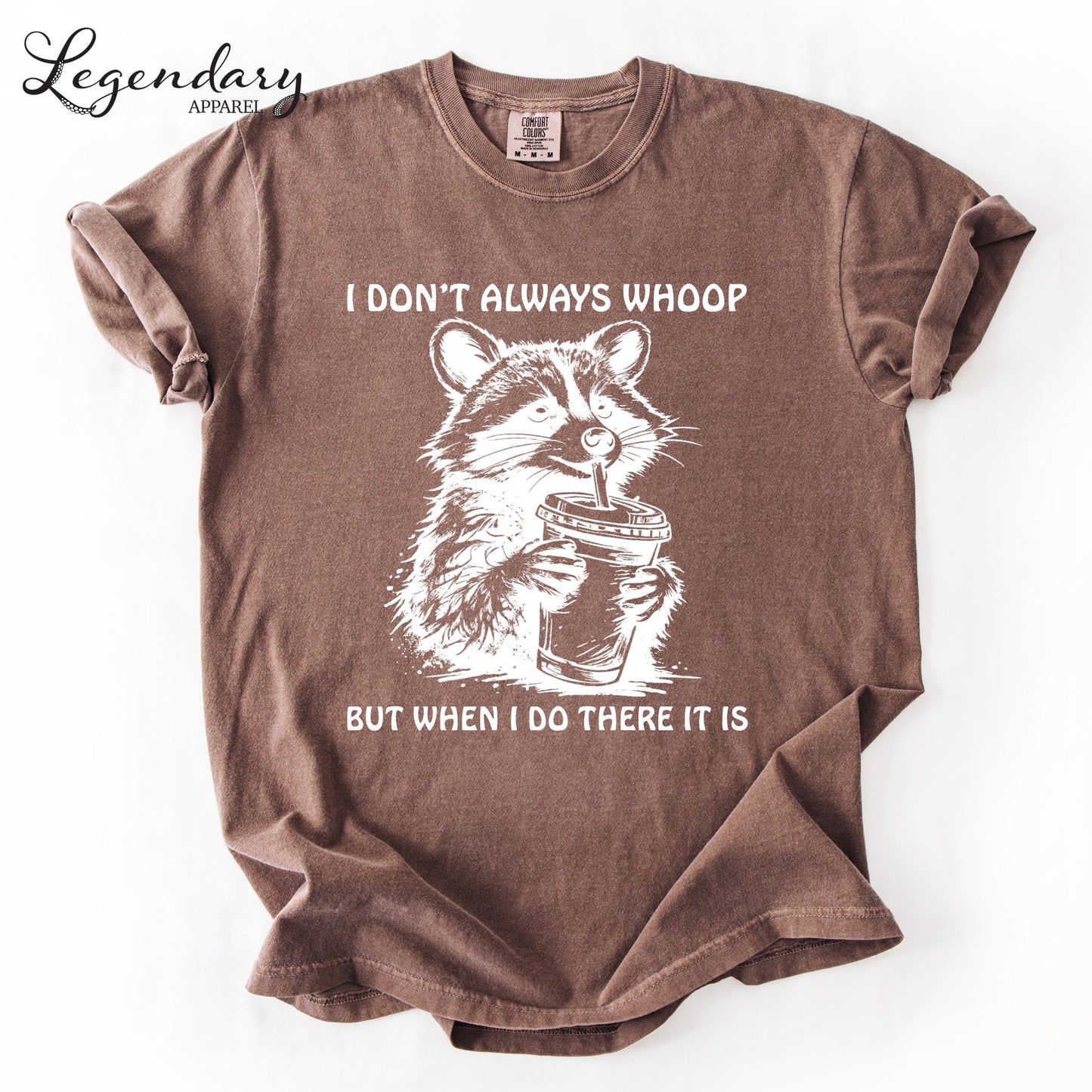 A brown t-shirt with a graphic design depicting a raccoon holding a cup, accompanied by the text "I DON'T ALWAYS WHOOP BUT WHEN I DO THERE IT IS".