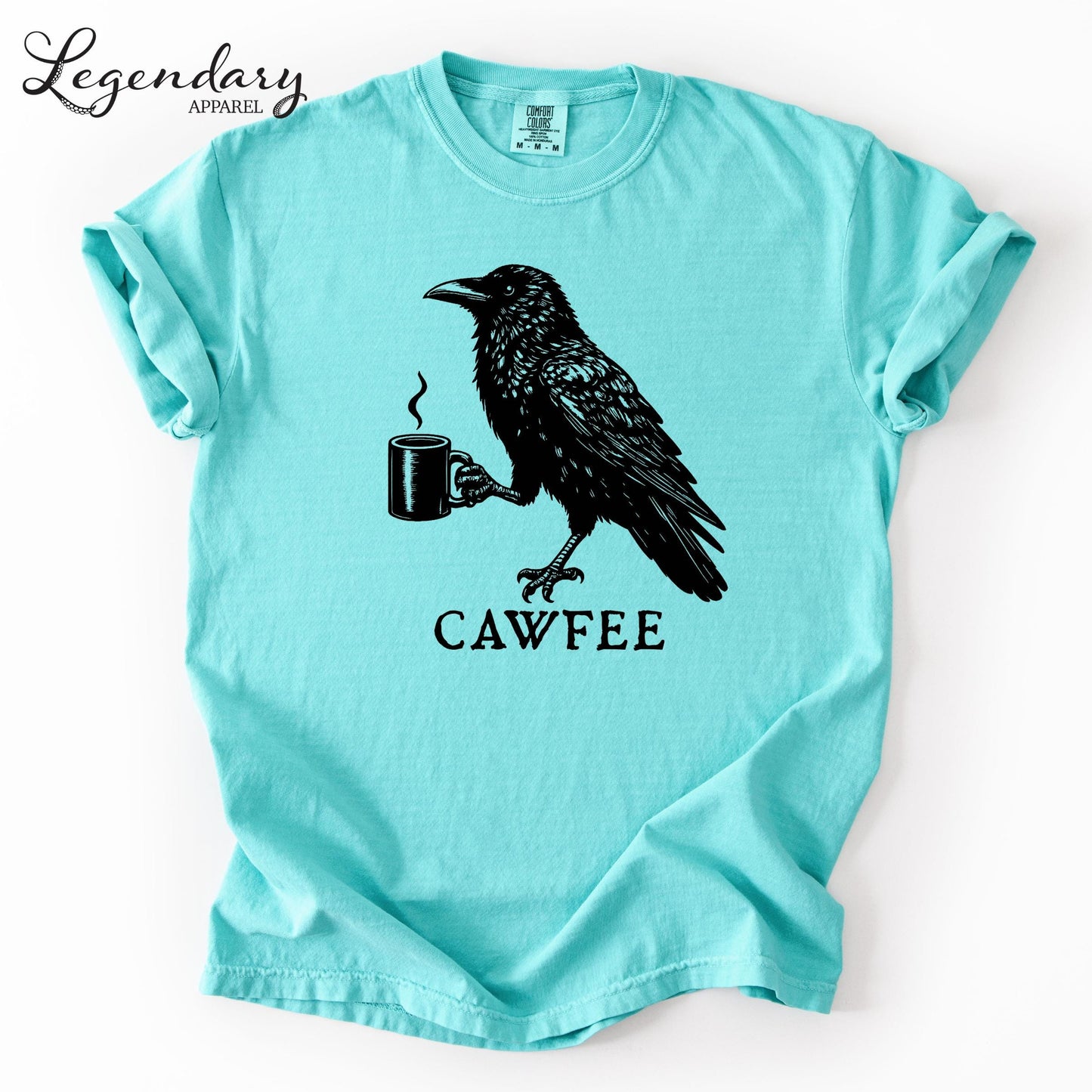 A turquoise t-shirt with a black illustration of a crow holding a coffee cup and the text "CAWFEE" below it.