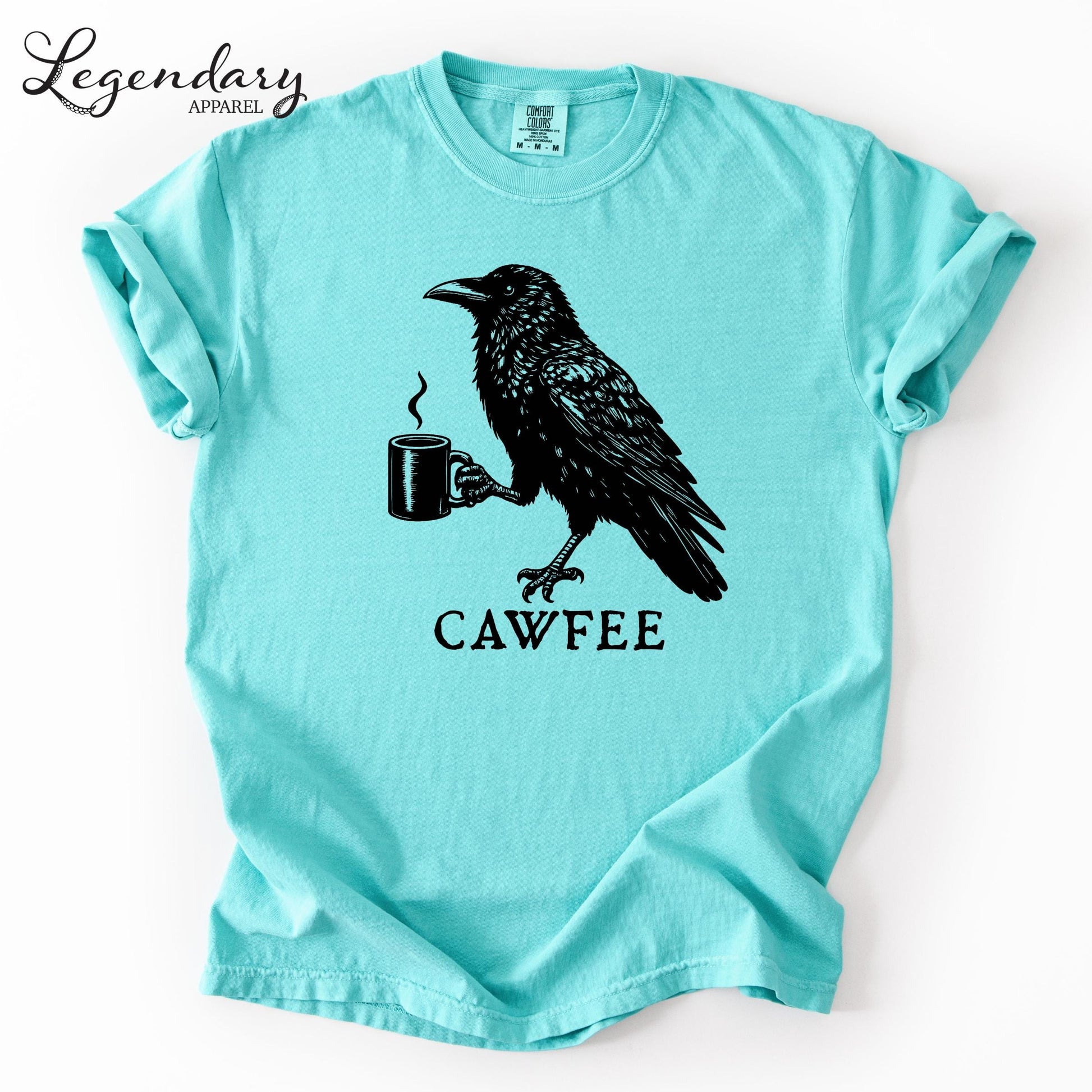 A turquoise t-shirt with a black illustration of a crow holding a coffee cup and the text "CAWFEE" below it.