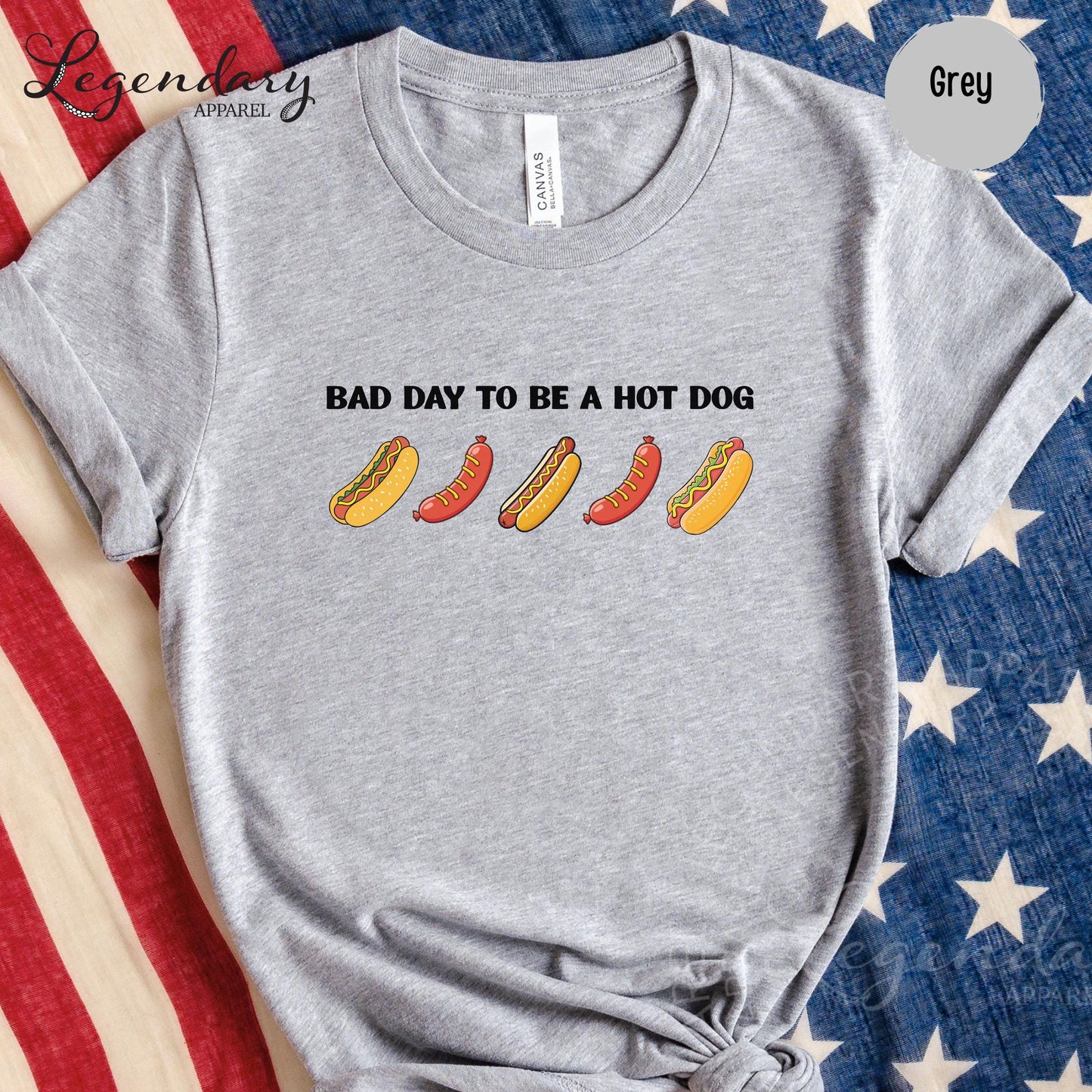 A grey t-shirt with a graphic design of five hot dogs in various colors and styles, along with the text "Bad day to be a hot dog".