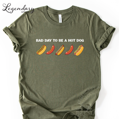 A green t-shirt with the text "Bad day to be a hot dog" printed on it, along with illustrations of hot dogs in various colors.
