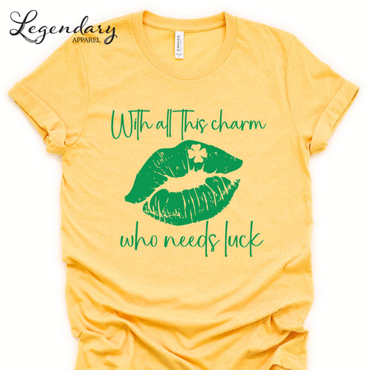 A yellow t-shirt with a graphic design featuring a pair of green lips with a clover on them, along with the text "With all this charm who needs luck".