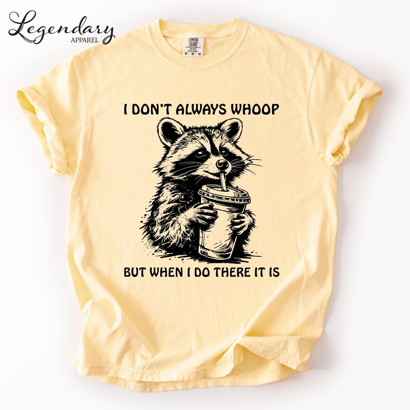 A yellow t-shirt with a graphic of a raccoon holding a cup and the text "I DON'T ALWAYS WHOOP BUT WHEN I DO THERE IT IS" printed on it.