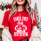 A woman wearing a red t-shirt with a graphic of Santa Claus and the text &quot;Santa says six seven&quot; printed on it.