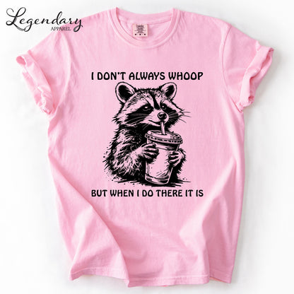 A pink t-shirt with a graphic design depicting a raccoon holding a cup, accompanied by the text "I DON'T ALWAYS WHOOP BUT WHEN I DO THERE IT IS".