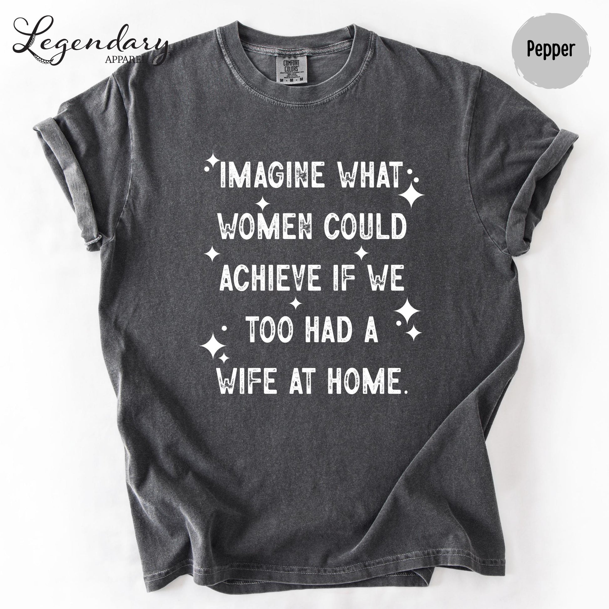 a gray t-shirt with white text printed on it. The text reads "IMAGINE WHAT WOMEN COULD ACHIEVE IF WE TOO HAD A WIFE AT HOME."