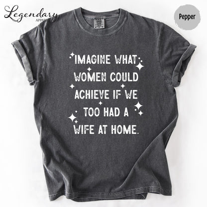 a gray t-shirt with white text printed on it. The text reads "IMAGINE WHAT WOMEN COULD ACHIEVE IF WE TOO HAD A WIFE AT HOME."
