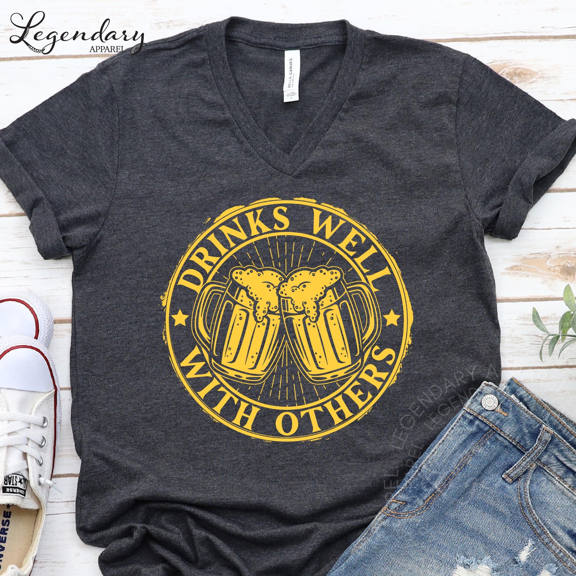 a gray t-shirt with a yellow graphic design that says "Drinks well with others" and a pair of blue jeans.