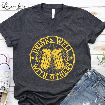 a gray t-shirt with a yellow graphic design that says "Drinks well with others" and a pair of blue jeans.